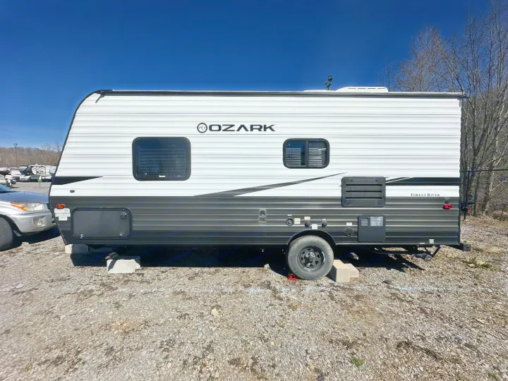 A white and dark grey Forest River Ozark travel trailer, parked on gravel under a clear blue sky, ideal for an RV rental.. Ozark Lite 2021