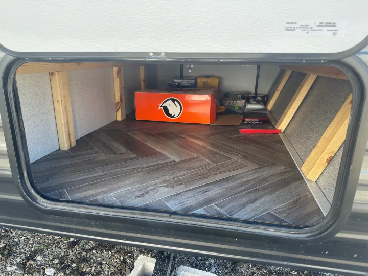 Spacious RV rental pass-through storage with herringbone floor, showcasing camping gear and sturdy wooden supports.. Ozark Lite 2021