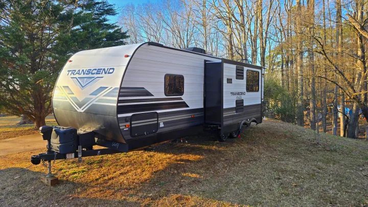 This RV rental, a white and black Transcend Xplor travel trailer, is parked on a sunny, grassy hill surrounded by trees.. Grand Design Transcend Xplor 2020