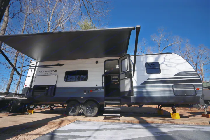 This white & grey RV rental is set up at a sunny campsite with its awning extended and outdoor kitchen ready. Perfect for camping.. Grand Design Transcend Xplor 2020