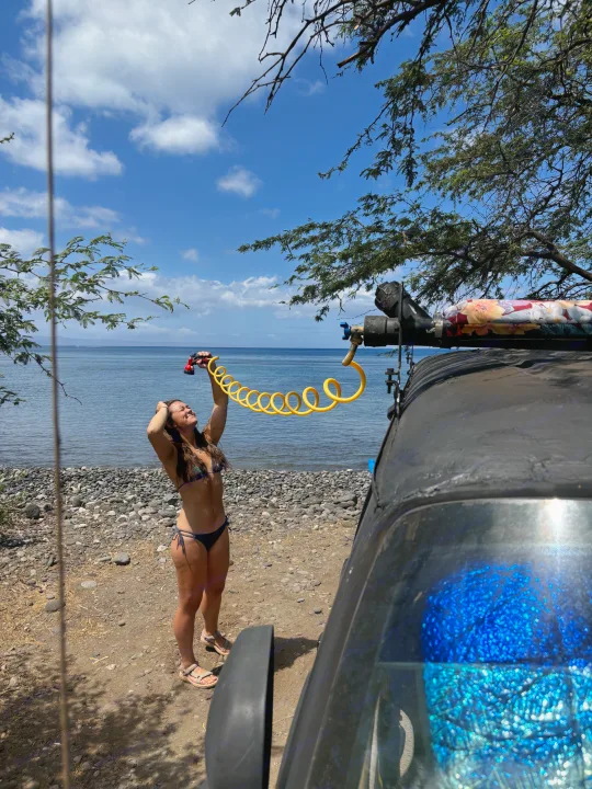 RV rental outdoor shower on a sunny beach. A woman in a bikini uses a yellow coiled hose by the sea.. Dodge 1500 1999