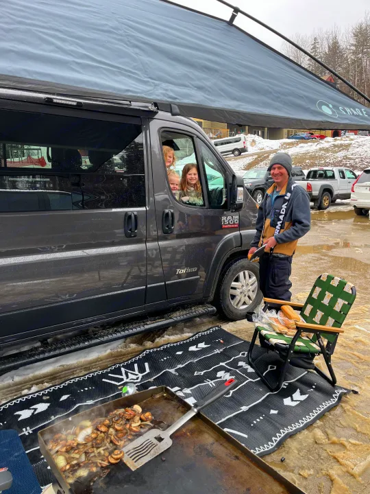 RV rental life: Kids in the van, man cooking on a griddle outside under an awning on a muddy/snowy day.. Pleasure-Way Pleasure-Way Class B 2022