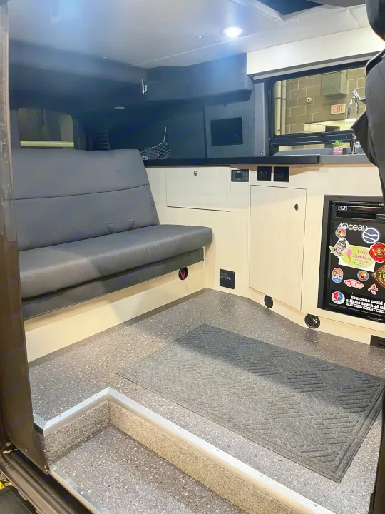 RV rental interior features a dark bench seat, light wood cabinets, and a compact kitchen area with fridge.. Pleasure-Way Pleasure-Way Class B 2022