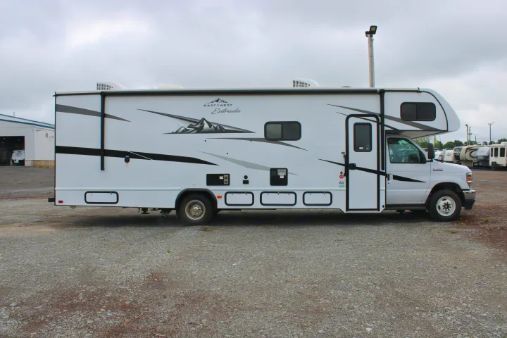 This white East West Entrada Class C RV is ready for rv rental adventures, parked on a gravel lot under an overcast sky.. East to West Entrada 2023
