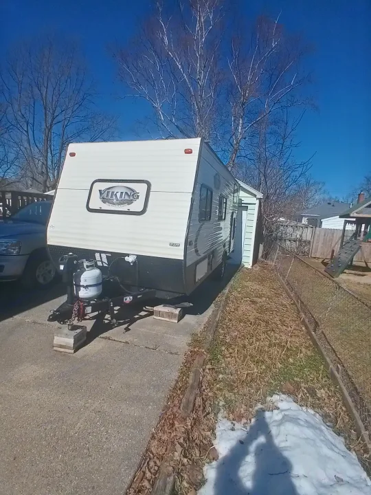A white Viking travel trailer, with propane tanks, is parked on a paved driveway, possibly for an RV rental, under a blue sky.. Coachmen Viking 2017