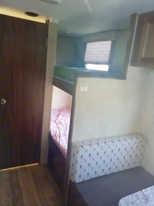 Cozy RV rental interior showcasing bunk beds with a window, a patterned dinette bench, and a dark wooden door.. Coachmen Viking 2017