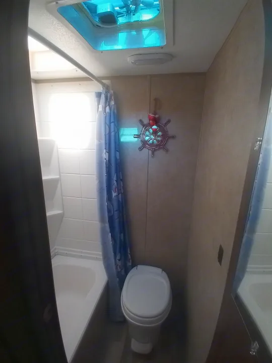 Compact RV rental bathroom: shower/tub, toilet, nautical wall decor, and blue ceiling vent for airflow.. Coachmen Viking 2017