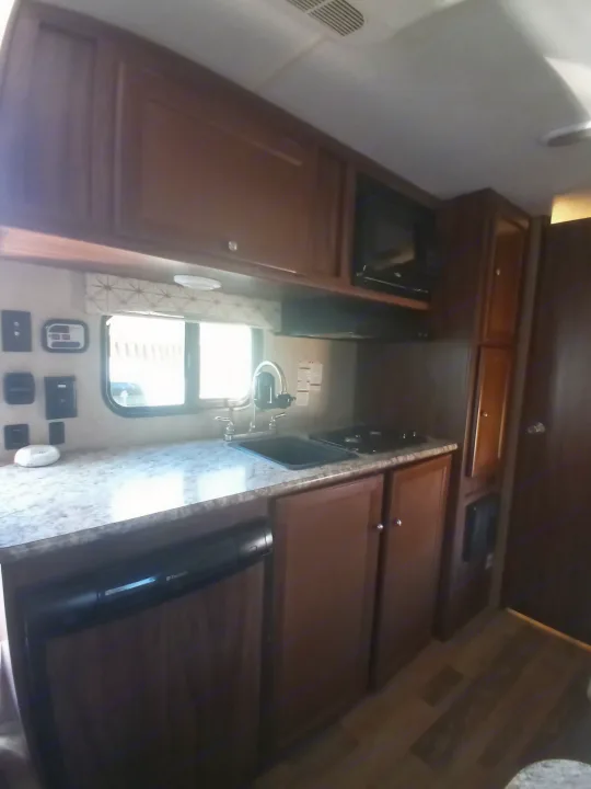 Modern RV rental kitchen with dark wood cabinets, bright countertops, sink, stovetop, microwave, and Dometic fridge.. Coachmen Viking 2017