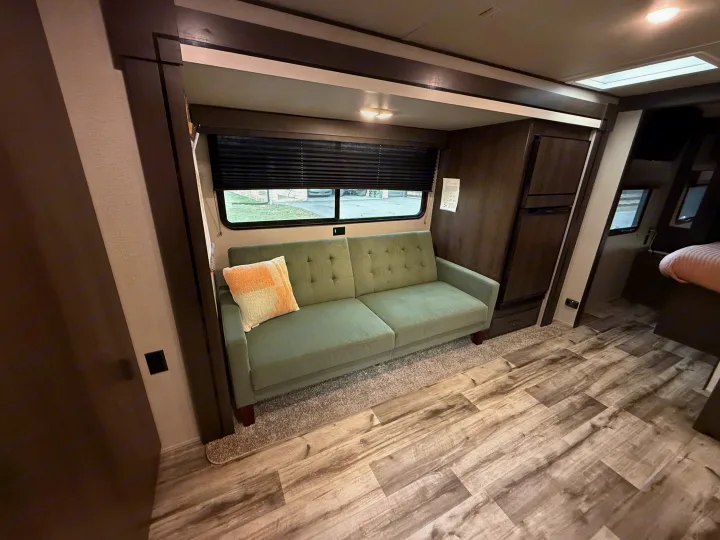 Inside an RV rental: a cozy living area with a plush green sofa, large window, and wood-look flooring. Modern and inviting.. Grand Design Transcend Xplor 2023