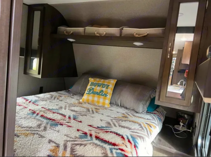 Cozy RV rental bedroom features a patterned bed, 'Howdy Darlin'' pillow, overhead storage, and mirrored cabinets.. Jayco Jay Flight SLX 2021
