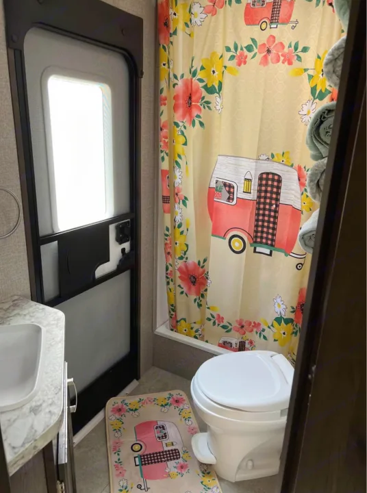 Experience comfort in this RV rental bathroom, featuring a themed shower curtain & mat, toilet, sink, and an exterior door.. Jayco Jay Flight SLX 2021
