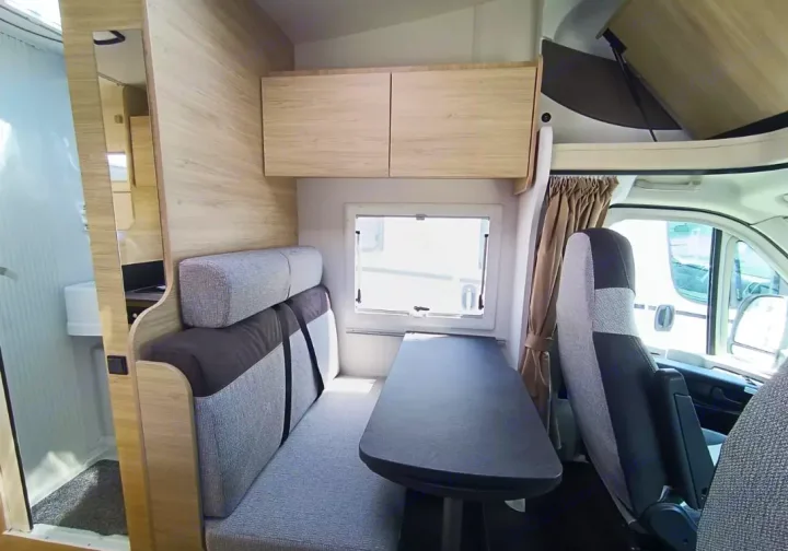 Modern RV rental interior: dining area with bench seating, table, overhead storage, and partial bathroom visible.. Challenger C194 START EDITION 2025