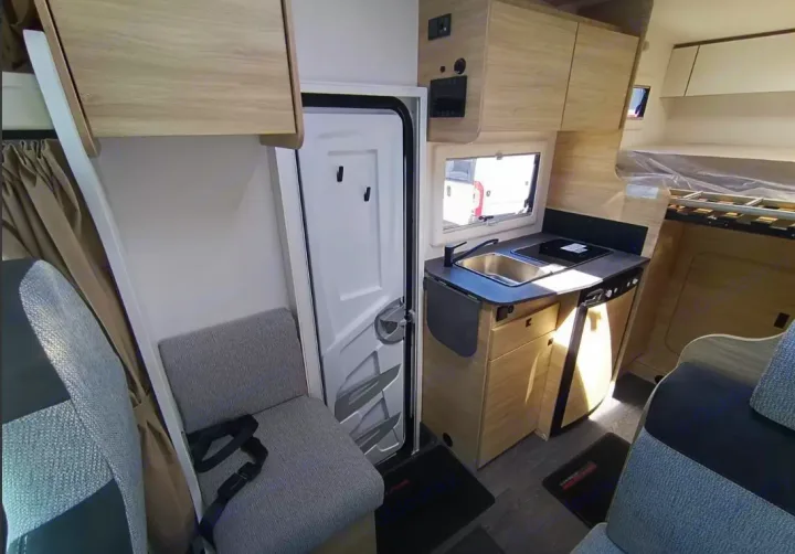 Modern rv rental interior showcasing a compact kitchen with sink/stove, comfortable seating with a seatbelt, and a cozy bed.. Challenger C194 START EDITION 2025