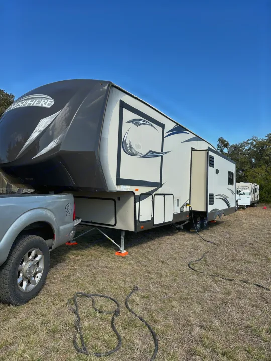 Fifth-wheel RV rental, connected to a truck, set up for camping with visible hookups on dry grass under a clear sky.. Forest River Salem Hemisphere Lite 2015