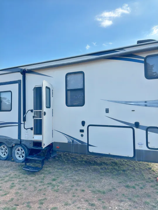 White RV rental parked outdoors, showing its side profile, open entry door, steps, and windows under blue sky.. Forest River Salem Hemisphere Lite 2015