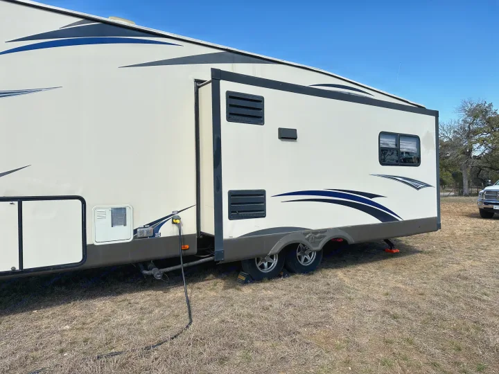 Side view of an rv rental: a white camper trailer with blue decals, slide-out extended, parked on dry ground at a campsite.. Forest River Salem Hemisphere Lite 2015