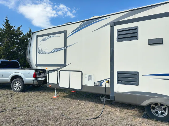 This large fifth-wheel RV rental is parked outdoors with a pickup truck attached, connected to power, under a blue sky.. Forest River Salem Hemisphere Lite 2015