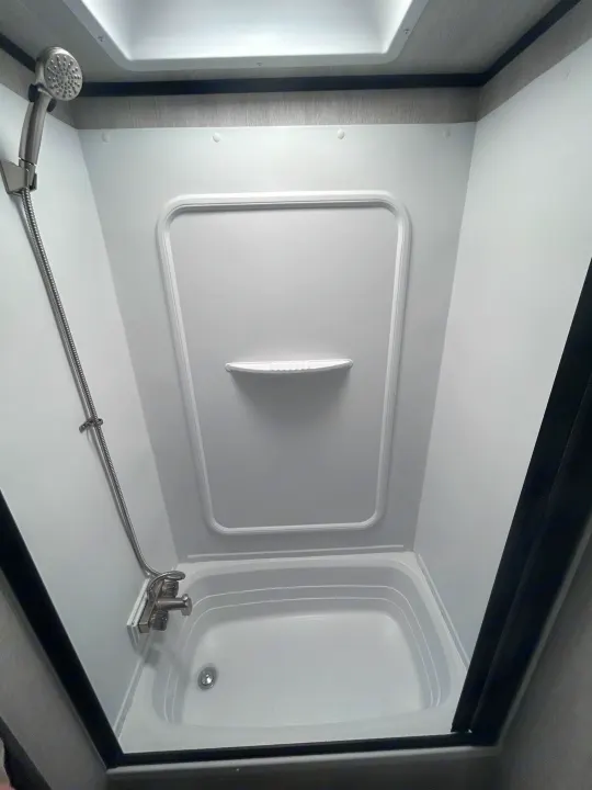 Bright, compact shower in an RV rental, with a white tub, handheld showerhead, and built-in shelf.. Genesis Supreme 16 BB 2024