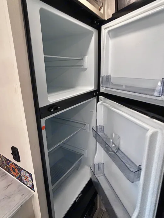 Clean, empty two-door RV refrigerator interior, ready for your RV rental trip. Features transparent shelves and door bins.. Genesis Supreme 16 BB 2024