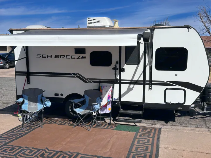 Relaxing setup: a white Sea Breeze RV rental with awning extended, two chairs, and rug ready for a getaway.. Genesis Supreme 16 BB 2024