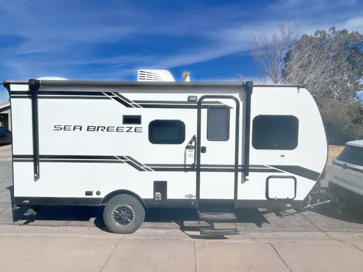 A sleek white "Sea Breeze" travel trailer, a compact RV with black accents and steps, ready for your next rv rental adventure.. Genesis Supreme 16 BB 2024