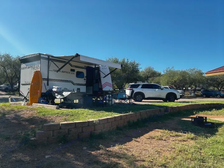 Sunny RV rental setup at a campsite. Features a white travel trailer, yellow kayak, and outdoor living area. Perfect for camping!. Genesis Supreme 16 BB 2024