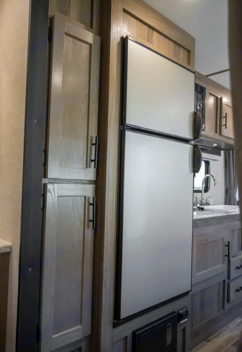 RV rental interior: practical kitchen featuring a two-door fridge, microwave, and light wood cabinetry for storage.. Gulf Stream 248BH 2022