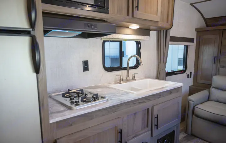 This RV rental showcases a compact kitchen with a two-burner stove, sink, refrigerator, and cozy armchair.. Gulf Stream 248BH 2022