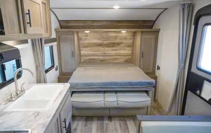 Inside this RV rental, see the cozy sleeping area with a bed, storage, and a kitchen counter with a sink.. Gulf Stream 248BH 2022
