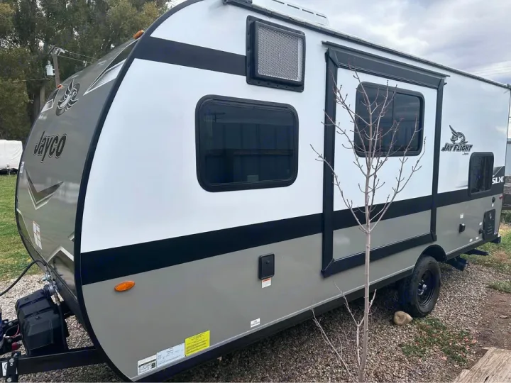 White & grey Jayco Jay Flight travel trailer RV rental parked outdoors on gravel. Compact & ready for adventure.. Jayco Jay Flight SLX 2024