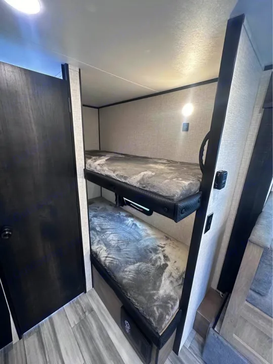 Cozy RV rental interior with two stacked bunk beds, featuring soft grey blankets and individual lighting, perfect for families.. Jayco Jay Flight SLX 2024