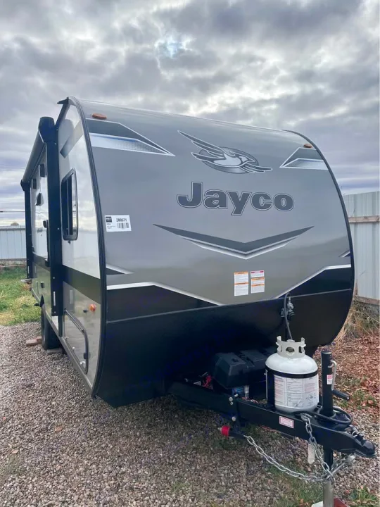Gray Jayco travel trailer, ideal for rv rental adventures. Features a propane tank and battery box on the hitch.. Jayco Jay Flight SLX 2024