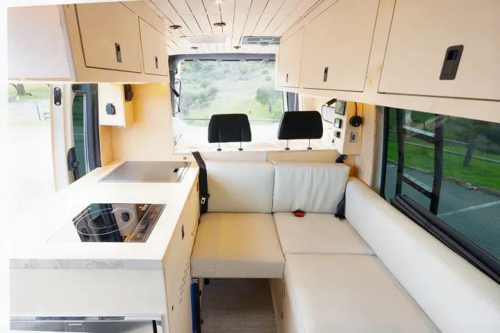 This cozy RV rental interior features a modern kitchenette, comfortable L-shaped seating, and smart overhead storage.. mercedes 144 High Roof AWD 2024