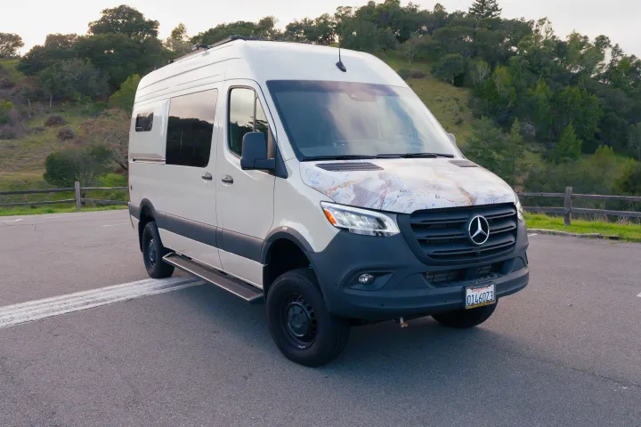 White Mercedes Sprinter rv rental, a customized camper van with a map-designed hood, parked in nature.. mercedes 144 High Roof AWD 2024
