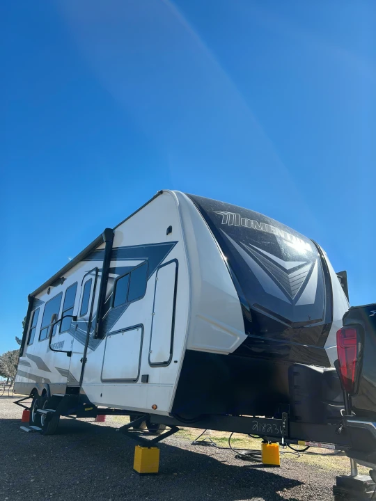 Experience outdoor leisure with this Momentum RV rental, a large white & black travel trailer parked under a sunny blue sky.. Grand Design Momentum Toy Hauler 2022