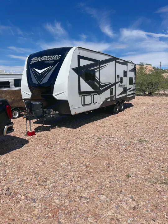 Grand Design Momentum RV on a gravel lot under a blue sky. Ideal for your next rv rental adventure and outdoor exploration.. Grand Design Momentum Toy Hauler 2022