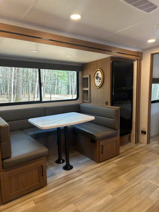 Cozy RV rental dinette and kitchen area with large windows showcasing a forest view.. Alliance RV Delta 251BH 2024