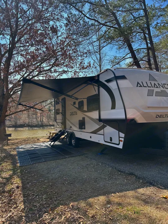 This Alliance Delta rv rental travel trailer offers a serene lakeside campsite with extended awning, perfect for your nature getaway.. Alliance RV Delta 251BH 2024