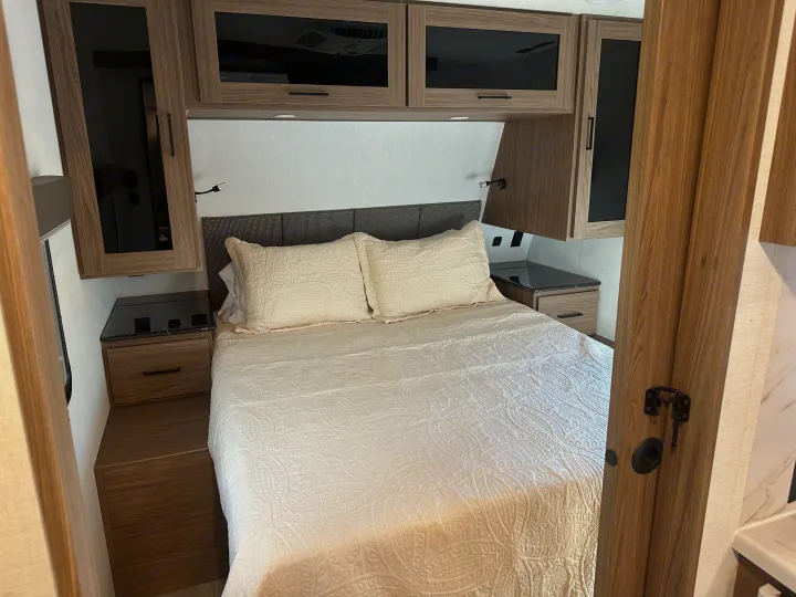 Inviting RV rental bedroom features a comfy bed, overhead cabinets, and practical nightstands for your travels.. Alliance RV Delta 251BH 2024