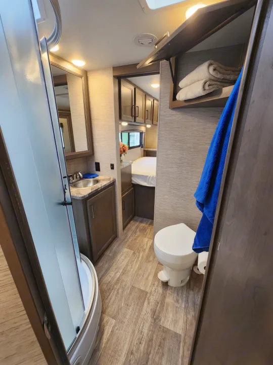 This RV rental offers a compact bathroom with a shower, toilet, and vanity, alongside a bed area and storage.. Thor Motor Coach Chateau 2023