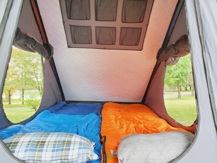 Inside a cozy RV rental: two sleeping bags and pillows, with a panoramic view of a park and lake.. Nissan XTerra 2012