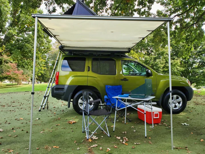 RV rental alternative: Green SUV with rooftop tent, awning, and camp kitchen set up for outdoor adventures.. Nissan XTerra 2012