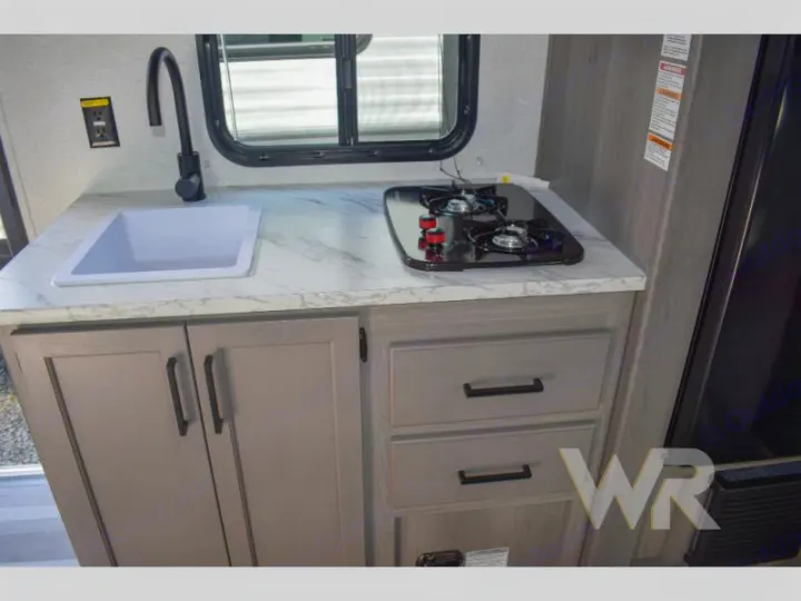 Compact RV rental kitchen featuring a sink, 2-burner stove, and light grey cabinets with a marble-look countertop.. Keystone RV Hideout Sport 2024