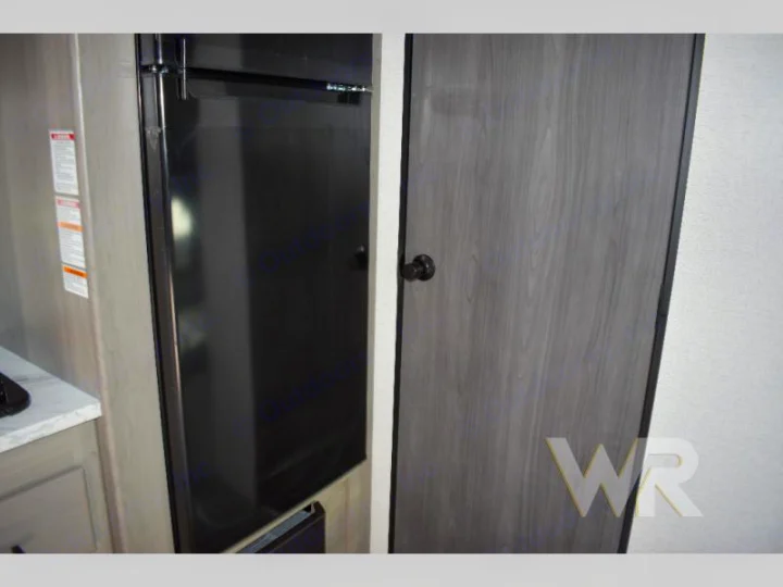 RV rental: Compact interior with a black refrigerator and a gray wood-look door with black hardware.. Keystone RV Hideout Sport 2024
