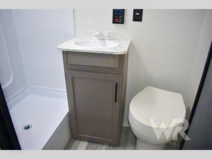 This RV rental bathroom includes a white sink on a vanity, a toilet, and a walk-in shower.. Keystone RV Hideout Sport 2024