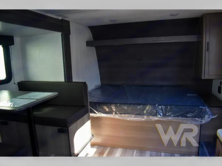 Inside an RV rental: a compact dinette booth and new bed with plastic wrap. Ready for travel.. Keystone RV Hideout Sport 2024