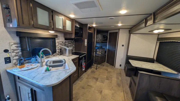 Spacious RV rental interior with a fully equipped kitchen, dining booth, and bunk beds, featuring modern wood finishes.. Dutchmen Coleman Lantern LT 2021