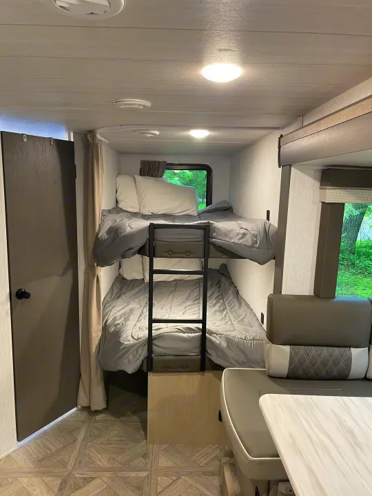 This inviting RV rental interior features comfy bunk beds, a dining area, and a window overlooking greenery.. Forest River Wildwood X-Lite Platinum 2024