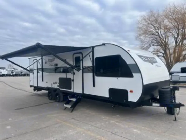 This modern white and black travel trailer, with its awning extended, is ready for your next RV rental adventure.. Forest River Wildwood X-Lite Platinum 2024