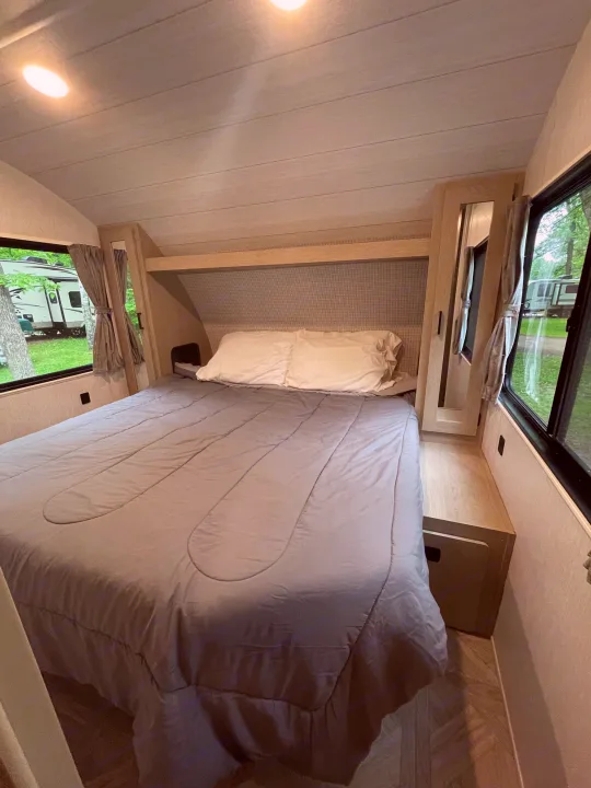 Relax in this RV rental's inviting bedroom, featuring a comfortable bed, mirrored wardrobes, and serene outdoor views.. Forest River Wildwood X-Lite Platinum 2024